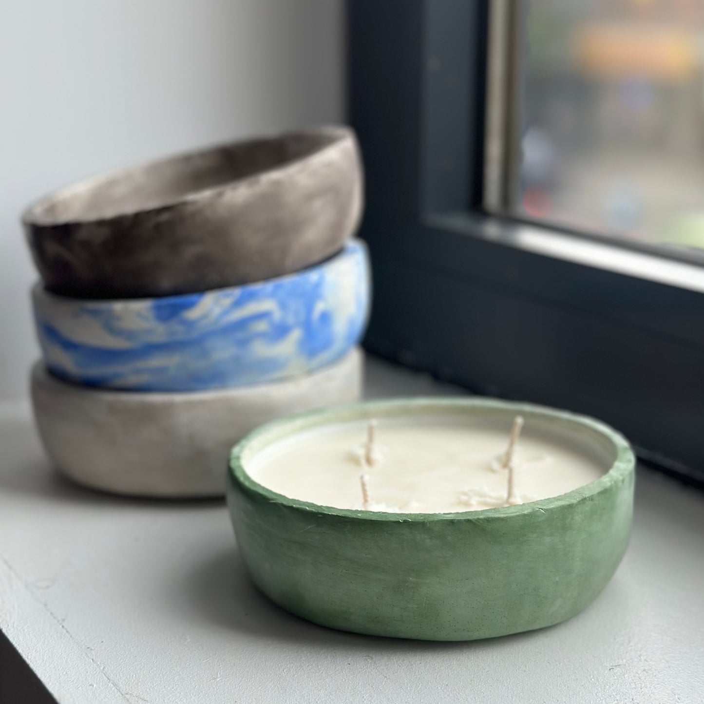 Stacked Various Concrete Decor Bowls on Window Sill and one Green Concrete Bowl with Candle.