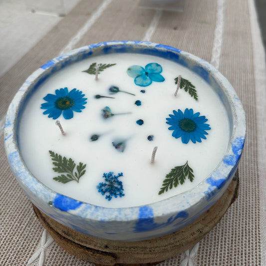 Blue and White Marble Concrete Container 12 Ounce Candle with Blue Dried Pressed Roses, Daisies, Hydrangea, Dill, and Baby's Breath Flowers on Display Table.