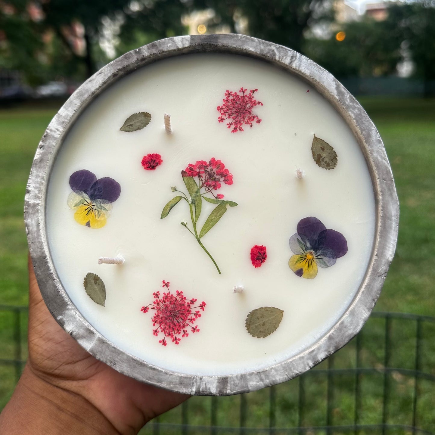 Dark Gray and White Marble Concrete 12 Ounce Candle with Dried Pressed Purple and Yellow Pansy, Red Dill, Red Baby's Breath and Red Yarrow and Sweet Assylum Flowers and Green Leaves held in Marcus Garvey Park, Harlem, New York City 